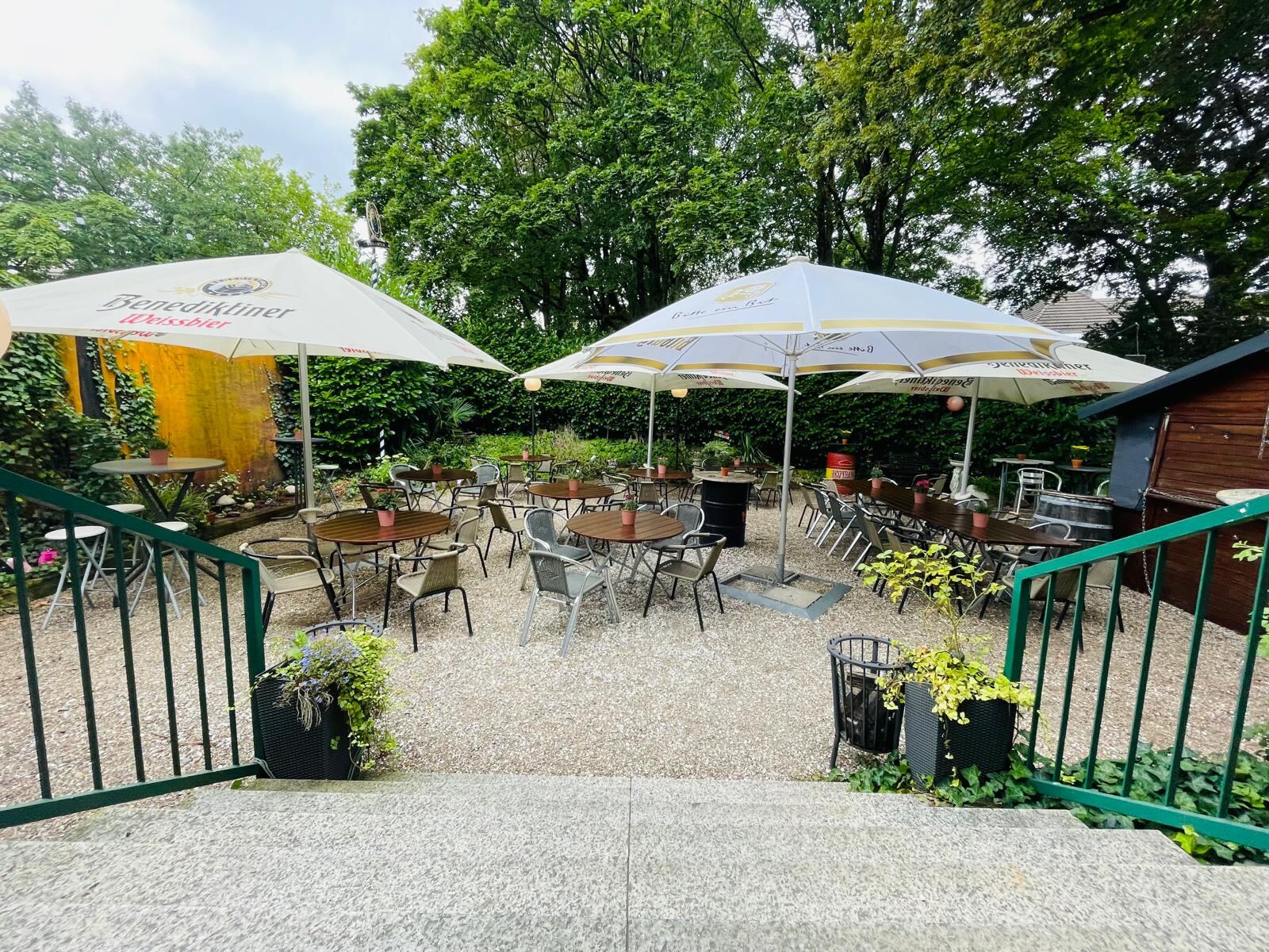 Biergarten des zum Verkauf stehenden Restaurants mit Sitzgruppen, Sonnenschirmen und dichtem Baumbestand