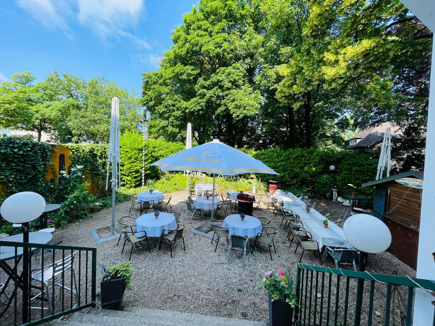 Biergarten des zum Verkauf stehenden Restaurants mit Sonnenschirmen und altem Baumbestand
